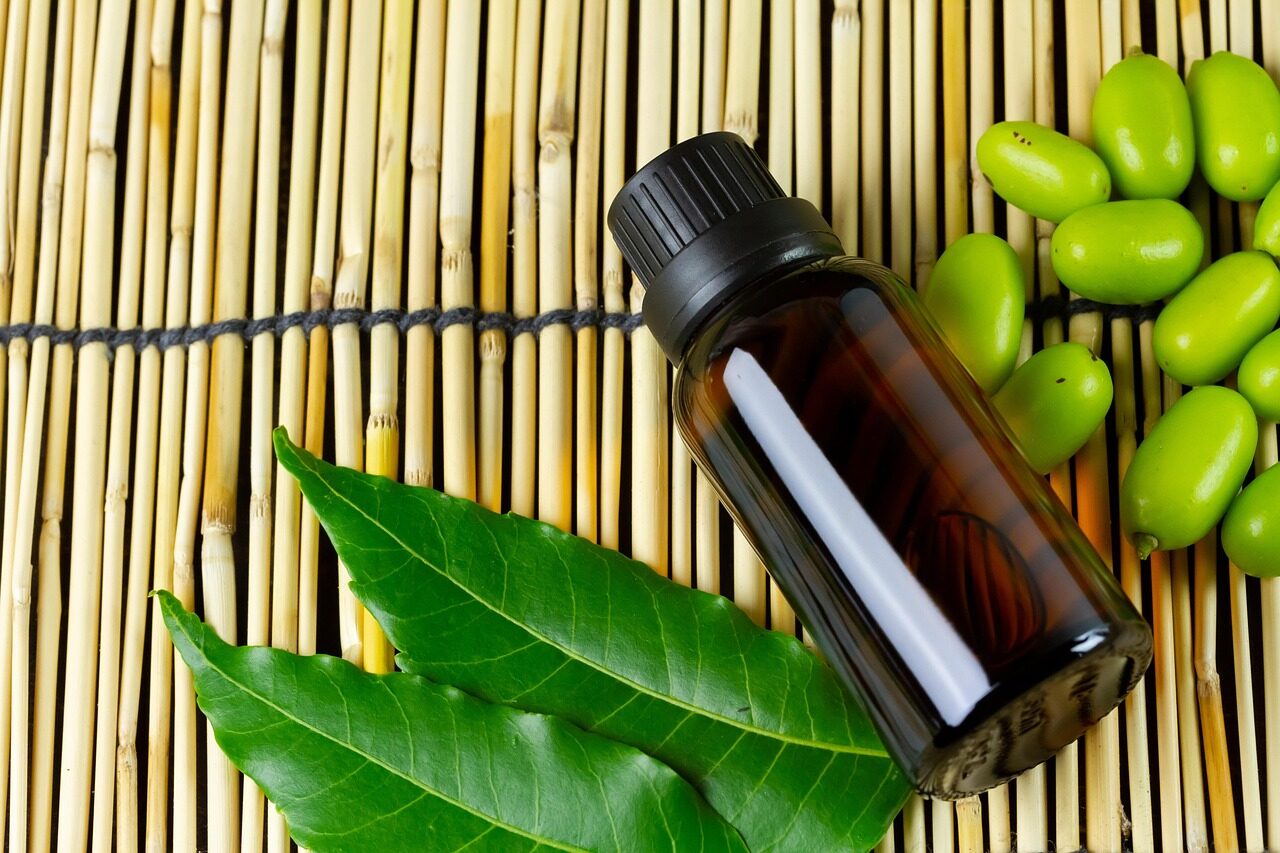 A dark amber bottle of neem oil with fresh neem leaves and green neem berries on a bamboo background