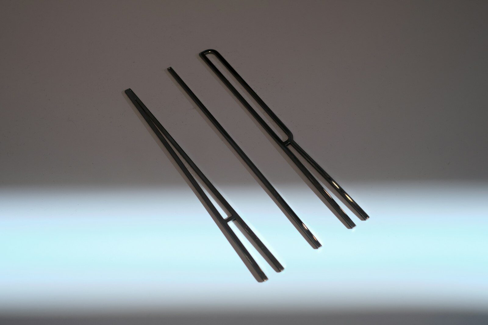 A set of dark matte black aquascaping tweezers and planting tools laid out on a neutral background